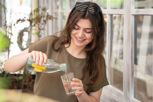 La giovane donna attraente beve l'acqua con il limone