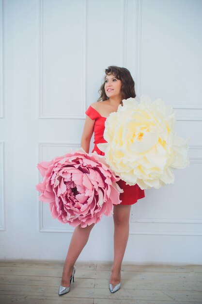 Foto attraente giovane donna in abito elegante interno decorato con fiori. bella ragazza sorridente fresca che posa con i fiori