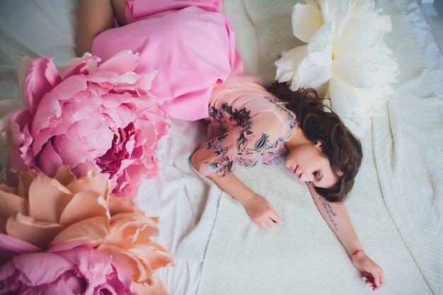 Attractive young woman in elegant dress sitting in interior decorated with flowers. Beautiful fresh smiling girl posing with flowers