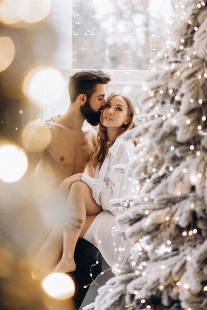 attractive young woman embracing shirtless boyfriend near christmas tree at home