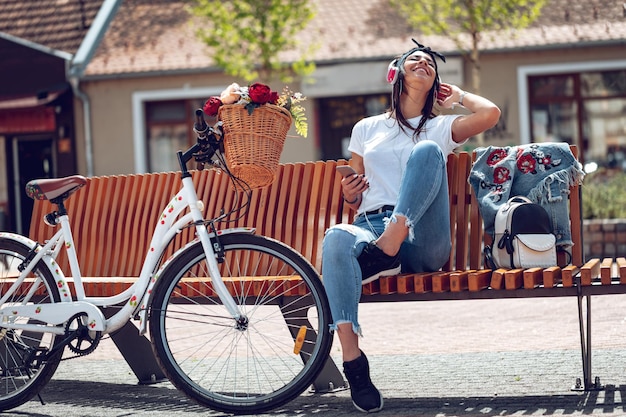 Photo attractive young woman finds the melody she like best, on the city street, during the stop of riding bike. she is glad of doing this.