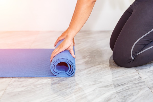 Attraente giovane donna pieghevole blu yoga o tappetino fitness dopo aver lavorato a casa in salotto