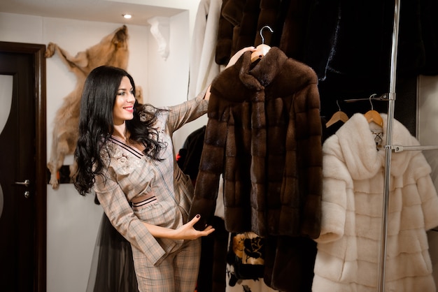 Attractive young woman in fur coat shop with a fur coats on the hanger