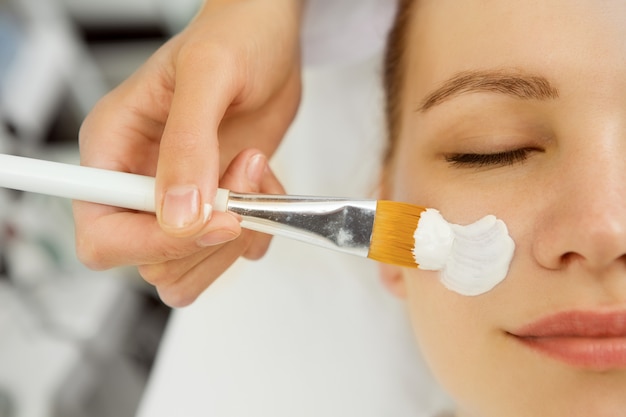 Attractive young woman getting facial mask at the spa