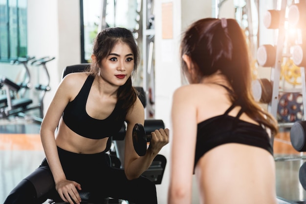 魅力的な若い女性ガラス ミラー ジムでダンベルでワークアウト