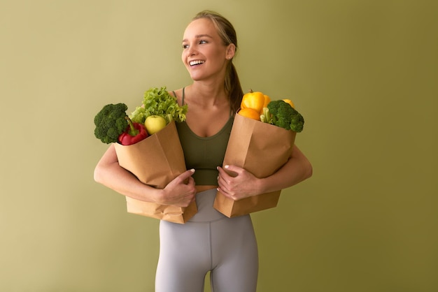 Привлекательная молодая женщина, держащая мешки с овощами на зеленом фоне Концепция здорового питания