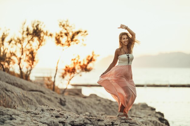 An attractive young woman is having fun and dancing while enjoying a summer vacation at the seaside.