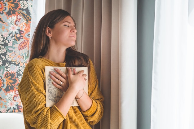 魅力的な若い女性は家で本を読んでいます。