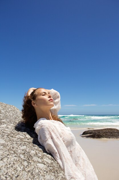 Attractive young woman leaning on rock at the beach