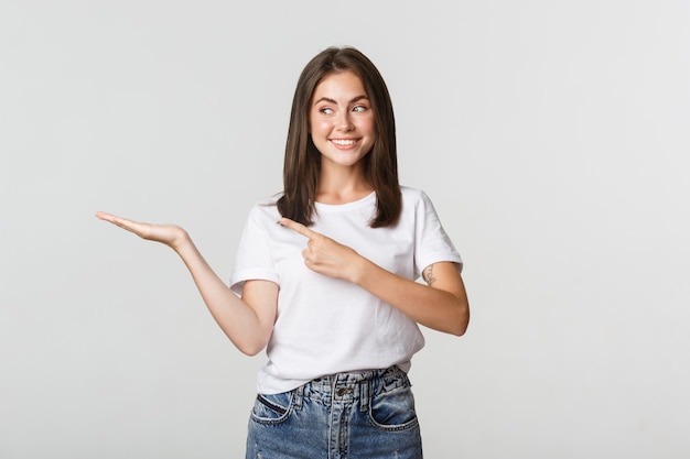 Attractive young woman pointing finger at something she holding on hand.