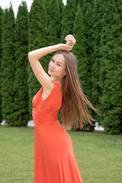 魅力的な若い女性が公園で赤いドレスでポーズ