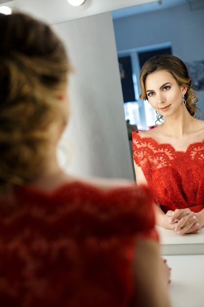 Attractive young woman in red dress is prepared in dressing room