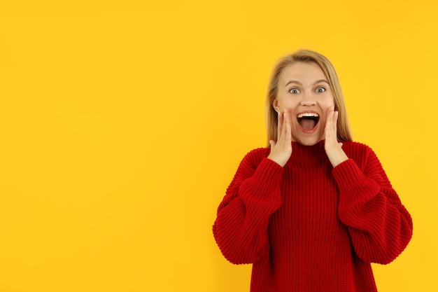 Attractive young woman in red sweater on yellow background.