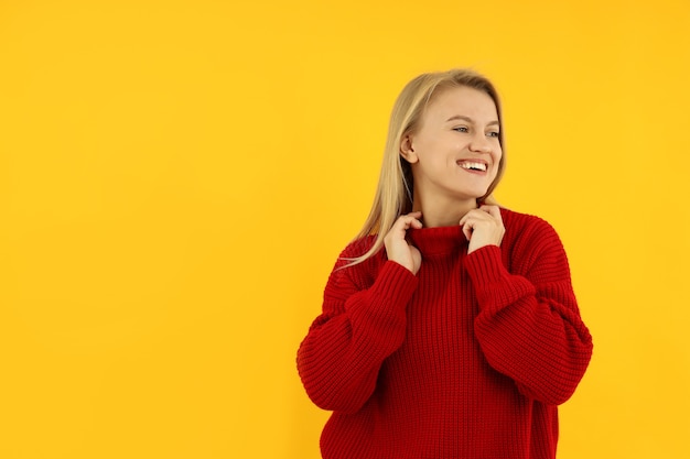 Attractive young woman in red sweater on yellow background.