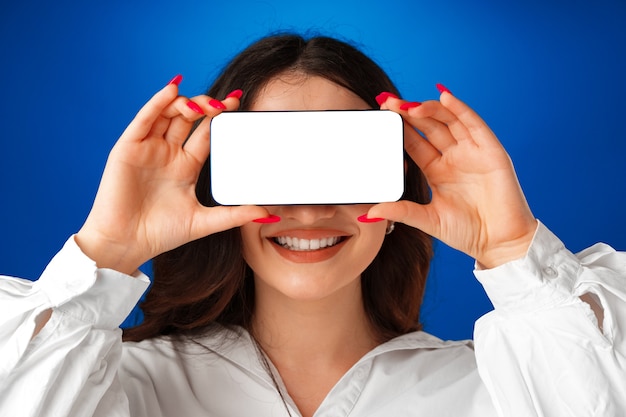 Attractive young woman showing blank smartphone screen with copy space