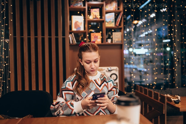 Attractive young woman sits at a table in a cafe with a cup of coffee and phone