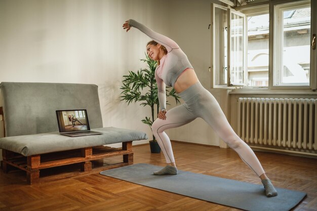 An attractive young woman sitting alone and stretching before a workout indoors.