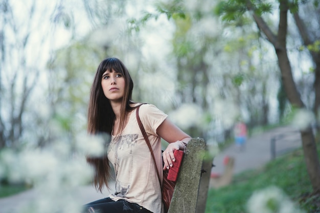 Photo attractive young woman sitting in a bench outdoors in the park