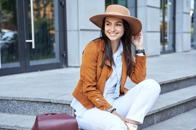 Attractive young woman sitting sitting on the steps and looking away in the city. Lifestyle concept