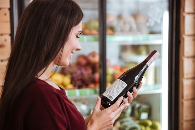 Attraente giovane donna in piedi e scegliendo il vino nel negozio di alimentari