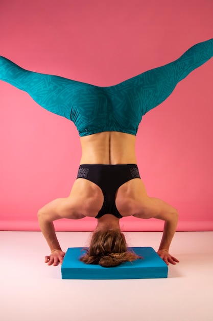 Attractive young woman standing on head, working out on the pink background. athletic girl doing exercise. strength and motivation, sport and healthy lifestyle, keep fit cocepts. female fitness