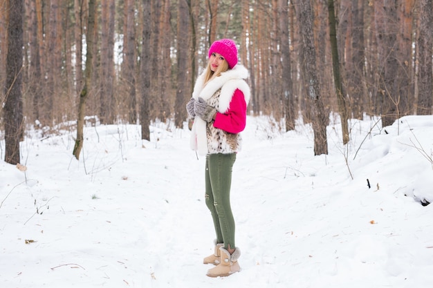 겨울 눈 덮인 공원에서 분홍색 따뜻한 재킷에 서있는 매력적인 젊은 여자