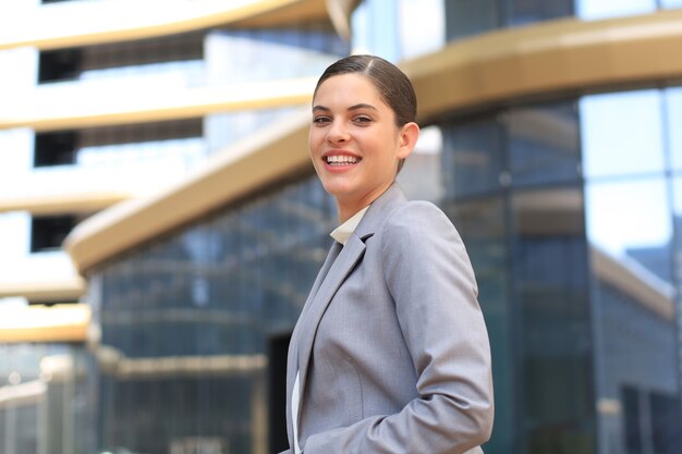 Attractive young woman in suit looking at camera and smiling while standing outdoors.