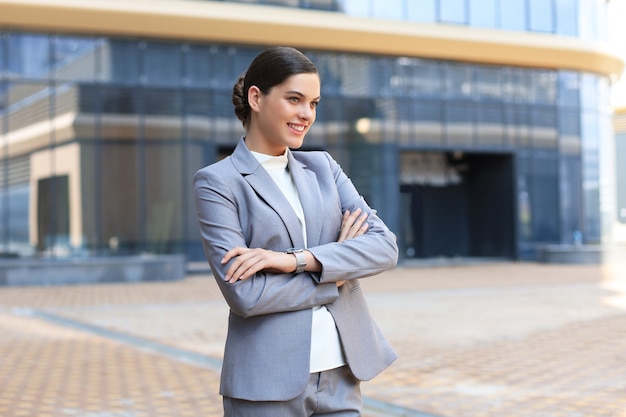 カメラを見て、屋外に立って笑っているスーツの魅力的な若い女性。