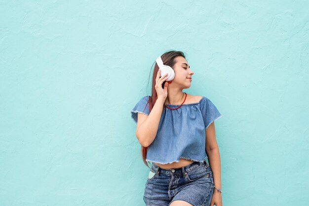 夏の服とサングラスを着た魅力的な若い女性が青い壁の音楽を聴いています