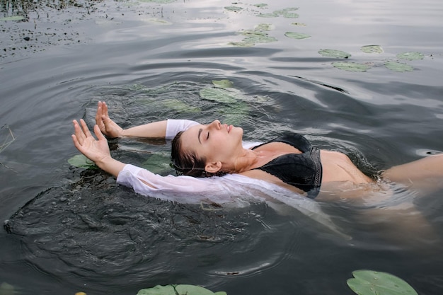 Foto attraente giovane donna che nuota in un lago tra belle ninfee in un costume da bagno nero