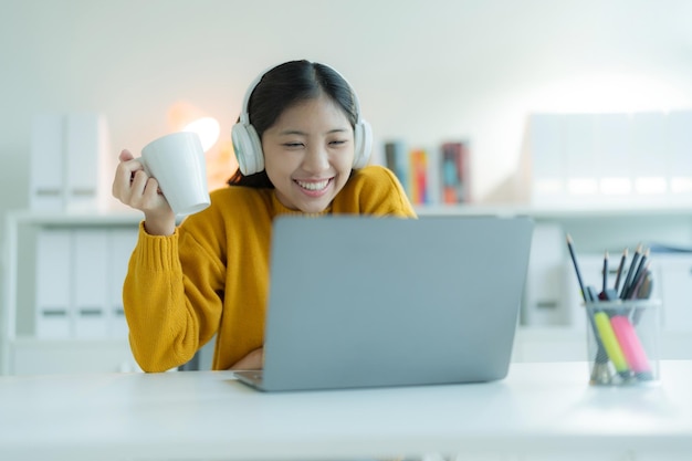 An attractive young woman uses a laptop computer in her home office with headphones smiling