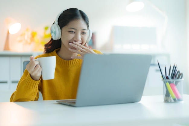 Photo an attractive young woman uses a laptop computer in her home office with headphones smiling