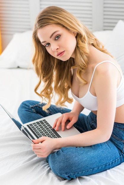привлекательная молодая женщина использует ноутбук в спальне