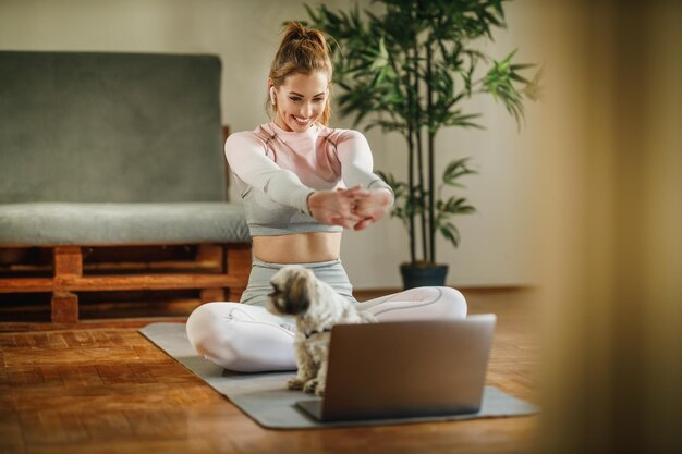 An attractive young woman using laptop to record her vlog about healthy living while doing exercises at home.