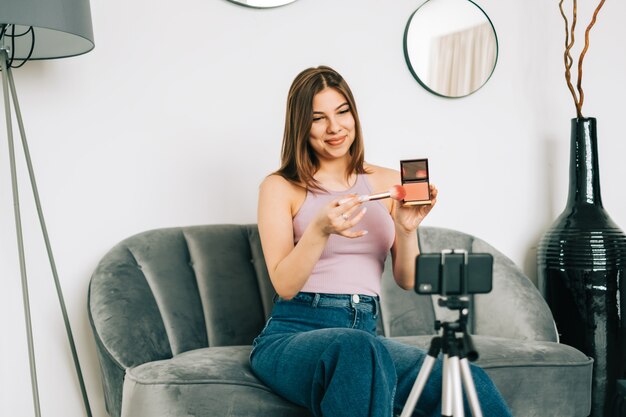 Attractive young woman video blogger showing beauty products via her blog on social media