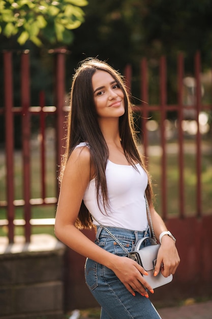 Foto attraente giovane donna che cammina in città nel periodo estivo bella bruna in camicia bianca sorriso