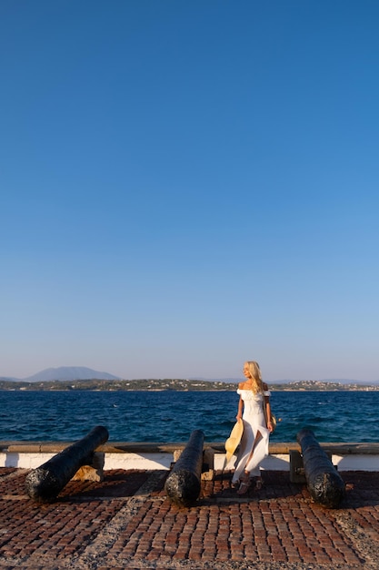 Attraente giovane donna che indossa un vestito in piedi in riva al mare con le mani alzate