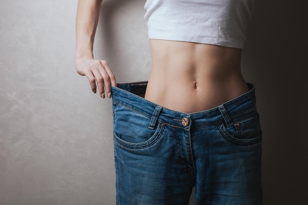 Attractive young woman wearing jeans and showing slim body after sport trainings and healthy eating