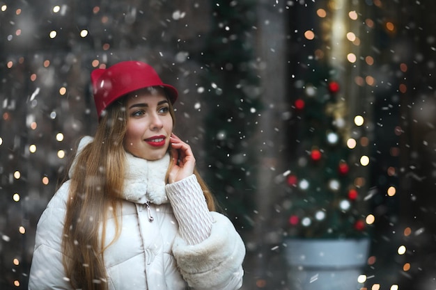 Attractive young woman wears red cap walking down the street decorated with garlands. Empty space
