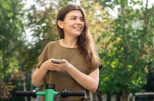 晴れた日にレンタル電動スクーターを持つ魅力的な若い女性