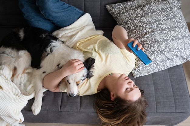 Attractive young woman with Australian shepherd typing in phone on couch.