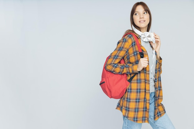 Attractive young woman with backpack on gray background place for text