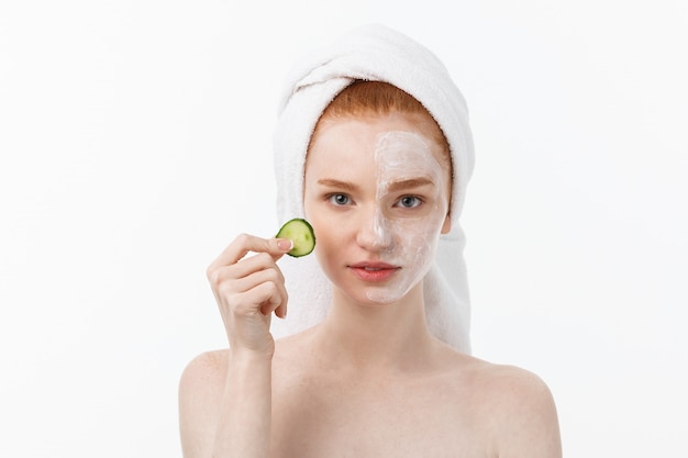 Attractive Young Woman with beautiful clean skin. White mask and cucumbers. Beauty treatments and cosmetology spa therapy. 