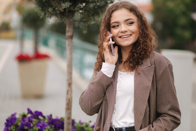 Attractive young woman with curly hair use phone in city Happy beautiful woman talk on the phone outdoors