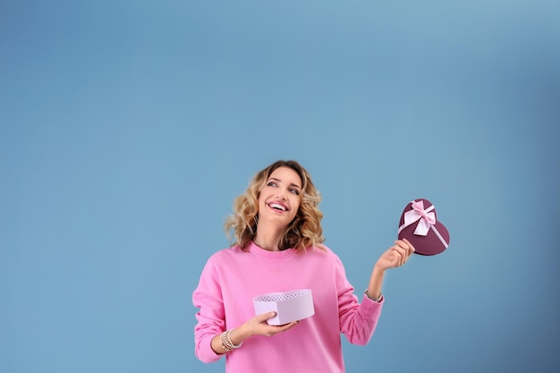 Attractive young woman with gift box on color background