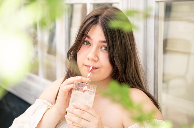 カフェテラスでレモネードのグラスを持つ魅力的な若い女性