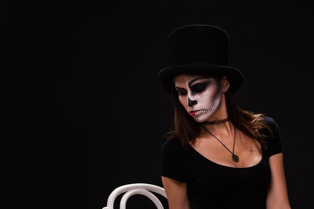 Attraente giovane donna con trucco gotico da vampiro sulla festa di halloween su sfondo nero halloween trucco viso