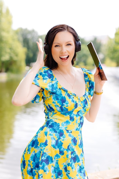 Attractive young woman with headphones listening to music via digital tablet a sunny day near lake