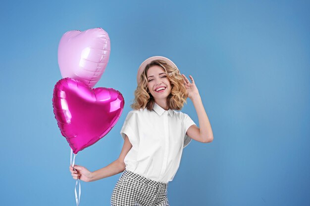 Attractive young woman with heart shaped air balloons on color background