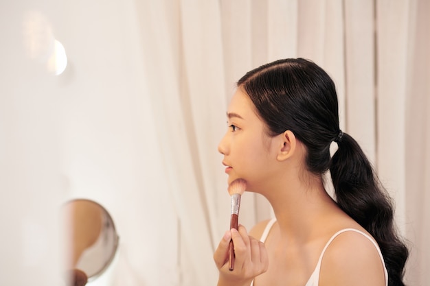 Привлекательная молодая женщина с макияжем, сделанным профессиональным художником, глядя в зеркало в помещении